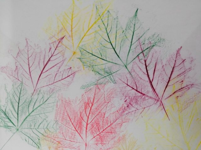 Kompozycja plastyczna struktur jesiennych liści w układzie symetrycznym. Praca wykonana w technice frotażu z użyciem barw ciepłych i zimnych.