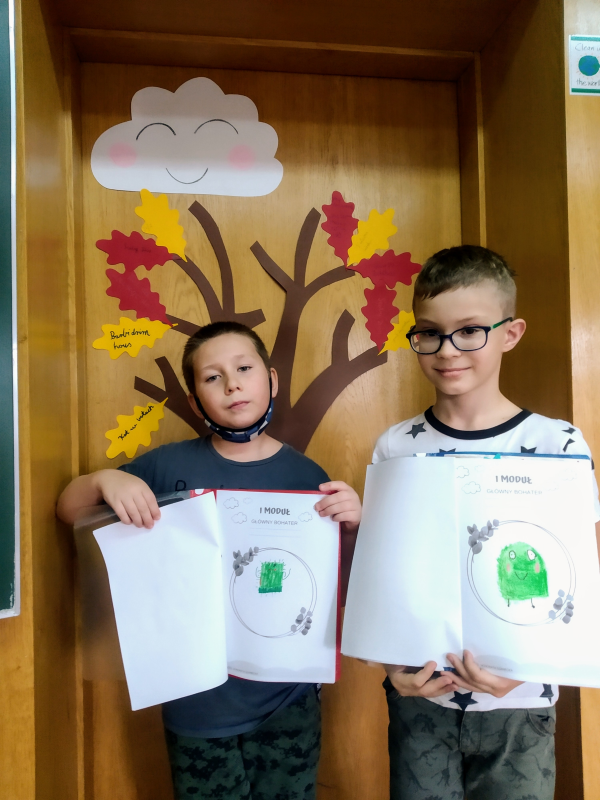 Chłopcy stoją na tle klasowego drzewa czytelniczego i prezentują narysowane w Lekturniku portrety Wystraszka