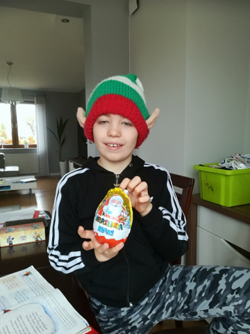 Szymon  z 2b w mikołajkowym stroju – czapka elfa i z upominkiem – Kinder jajo