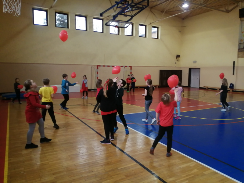 Dzieci rozproszone po sali odbijają balony na różne sposoby.
