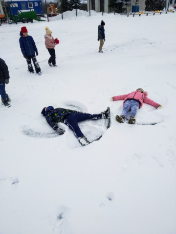 Dzieci leżą na śniegu i robią aniołki