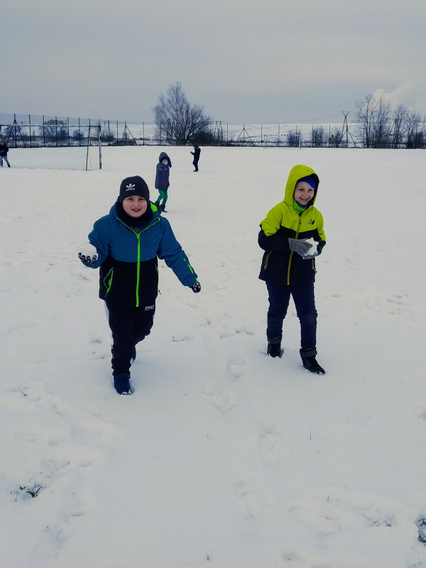 Chłopcy idą po śniegu trzymając w rękach śnieżki