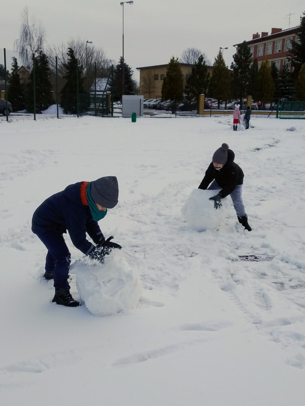 Chłopcy toczą ogromne kule ze śniegu