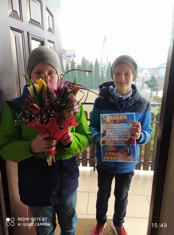 Na zdjęciu stoi dwóch chłopców. Jeden z nich trzyma kwiaty, a drugi dyplom. 