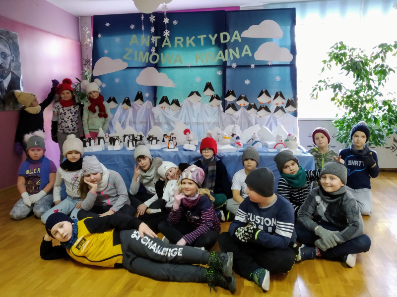 Grupowe zdjęcie dzieci z klasy II d na tle zimowej wystawy składającej się z bałwanków i pingwinów