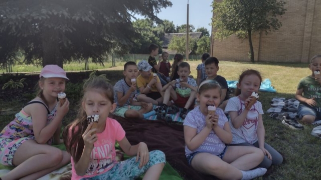 Dzieci siedzą na kocach i jedzą lody