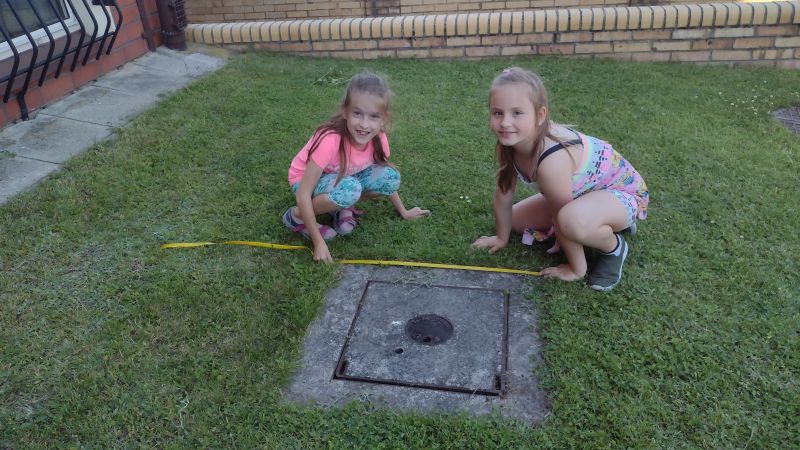 Dziewczynki mierzą długość betonowej studzienki.