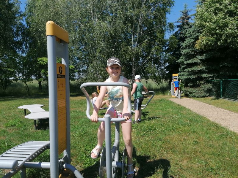 Dziewczynka ćwiczy na rowerku znajdującym się na siłowni zewnętrznej.