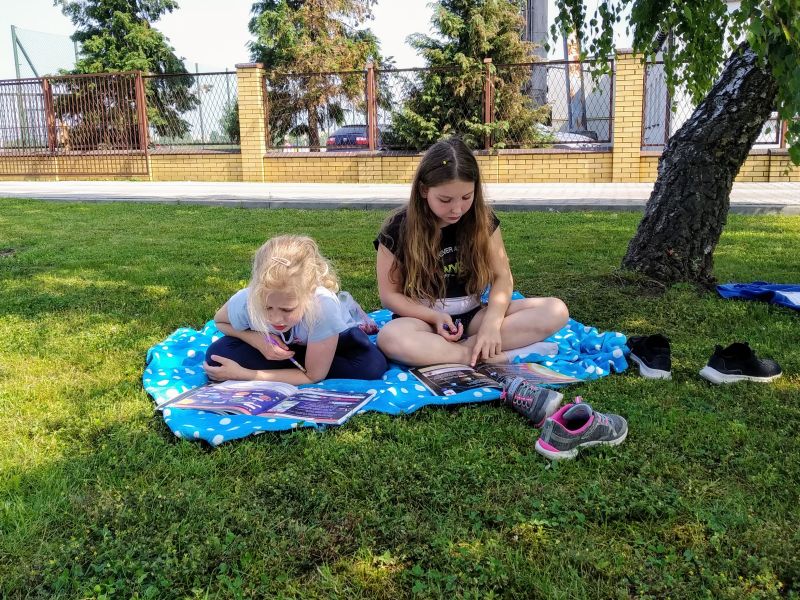 Dwie dziewczynki siedzą na kocu i rozwiązują zadania w książkach