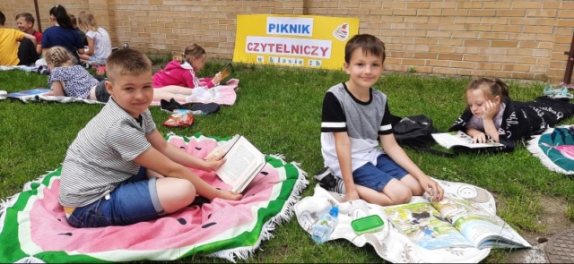 Piknik czytelniczy w 2b uczniowie na kocykach czytają przyniesione przez siebie książki