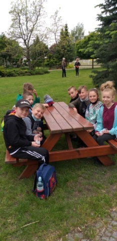 Uczniowie siedzą przy drewnianych stolikach na dworze
