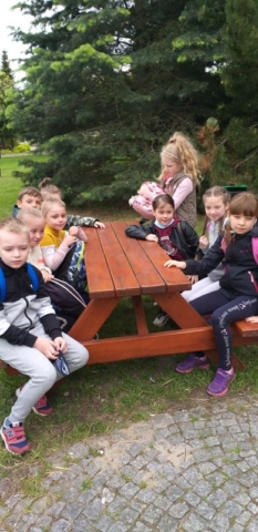 Uczniowie siedzą przy drewnianych stolikach na dworze