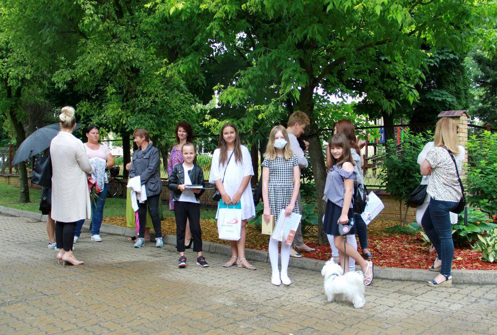 Grupa uczniów i rodziców stoi przed wejściem do szkoły