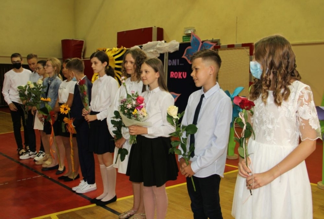 Uczniowie stoją w szeregu, trzymają kwiaty