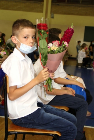 Uczeń siedzi na krześle, trzyma kwiaty