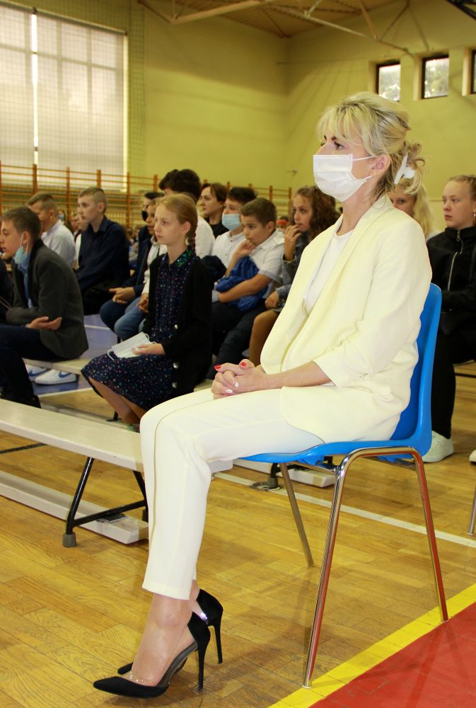 Nauczyciel siedzi w maseczce na twarzy, w tle uczniowie