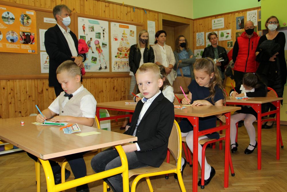 Uczniowie klas pierwszych siedzą w ławeczkach