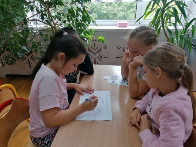 Uczniowie siedzą przy stoliku i podpisują miasta na mapie Polski.