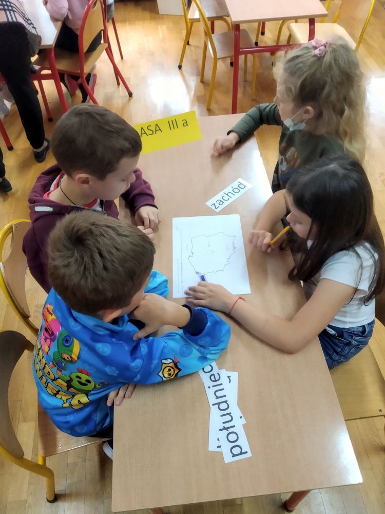 Dzieci układają nazwy kierunków geograficznych dookoła mapy.