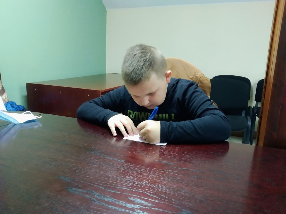 Chłopiec siedzi przy stoliku i wypisuje przelew.
