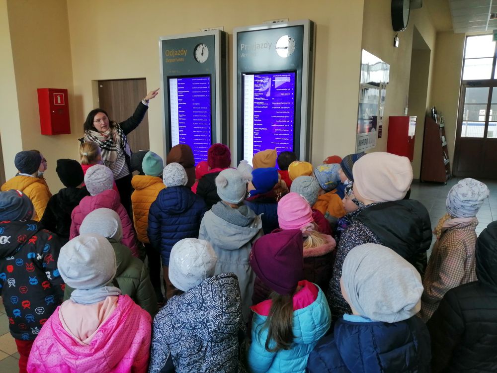 Nauczyciel prezentuje dzieciom rozkład jazdy pociągów na dworcu PKP w Radomsku.