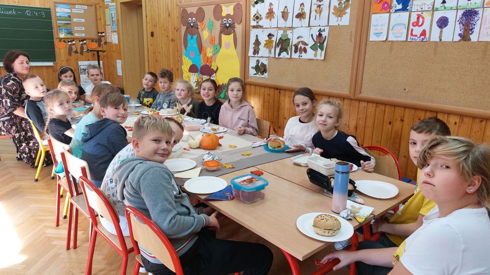 Uczniowie siedzą przy stole, jedzą wspólnie drugie śniadanie