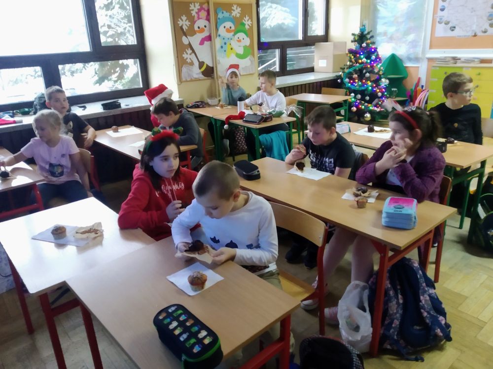 Uczniowie siedzą przy stolikach i jedzą babeczki