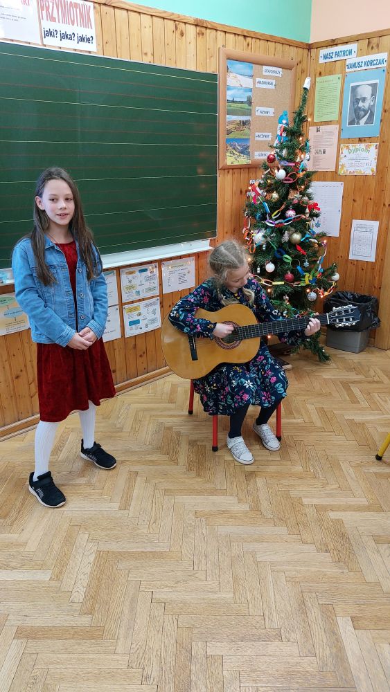 Dziewczynka gra na gitarze, a druga śpiewa kolędę