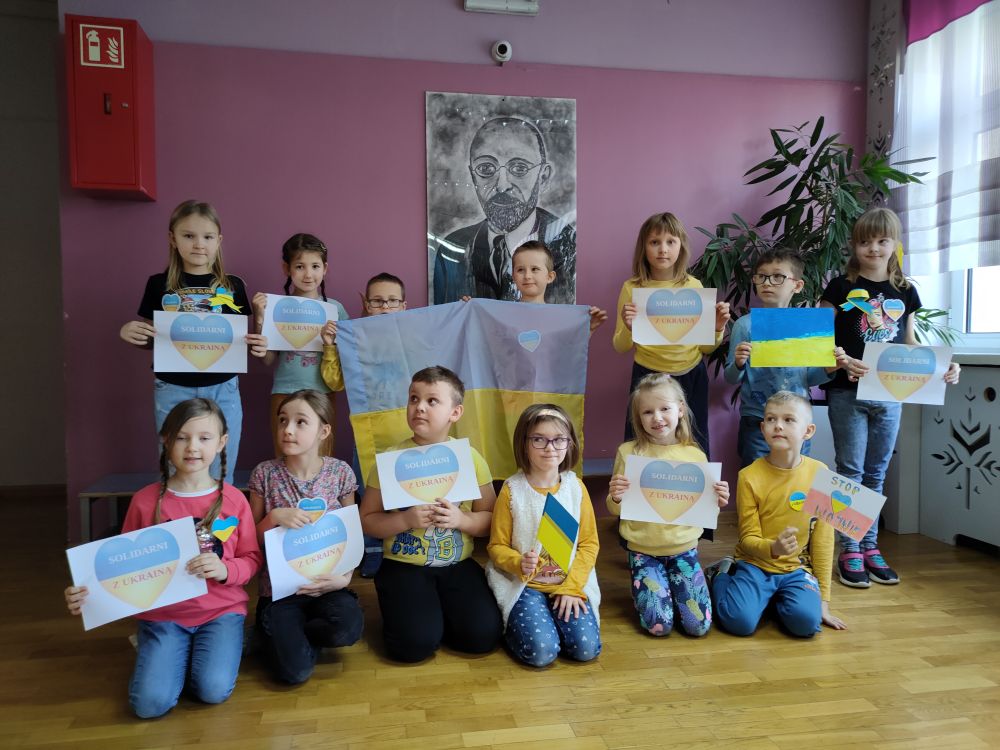 Dzieci stoją pod portretem Janusza Korczaka z pracami w barwach narodowych Ukrainy