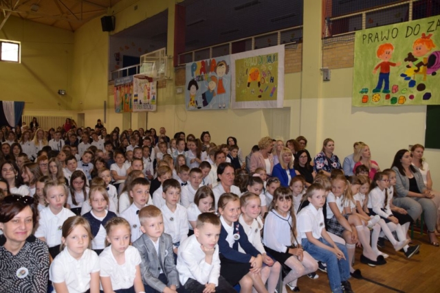 Społeczność szkolna i zaproszeni goście zgromadzeni na sali gimnastycznej w trakcie uroczystości.
