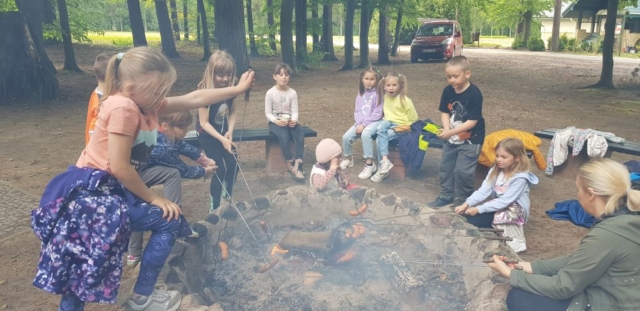 Dzieci pieką kiełbaski przy ognisku.