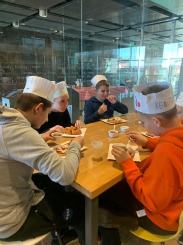 Uczniowie przy stole jedzą pizzę