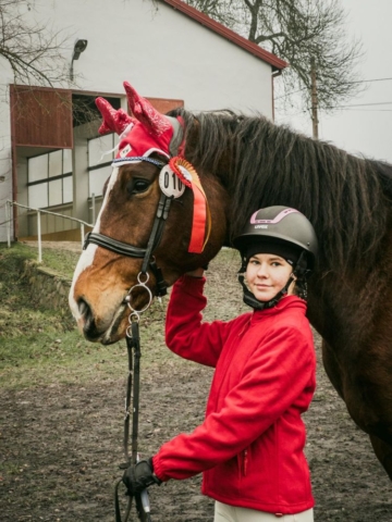 Dziewczyna stoi przy swoim koniu. Koń ma czerwone, świąteczne elementy ubioru.