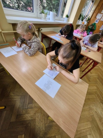 Uczniowie siedzą w ławkach i przepisują tekst