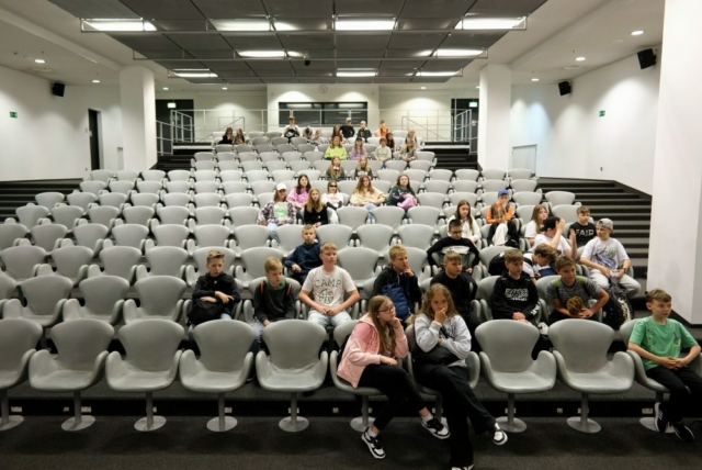Uczniowie siedzą w fotelach na sali konferencyjnej stadionu