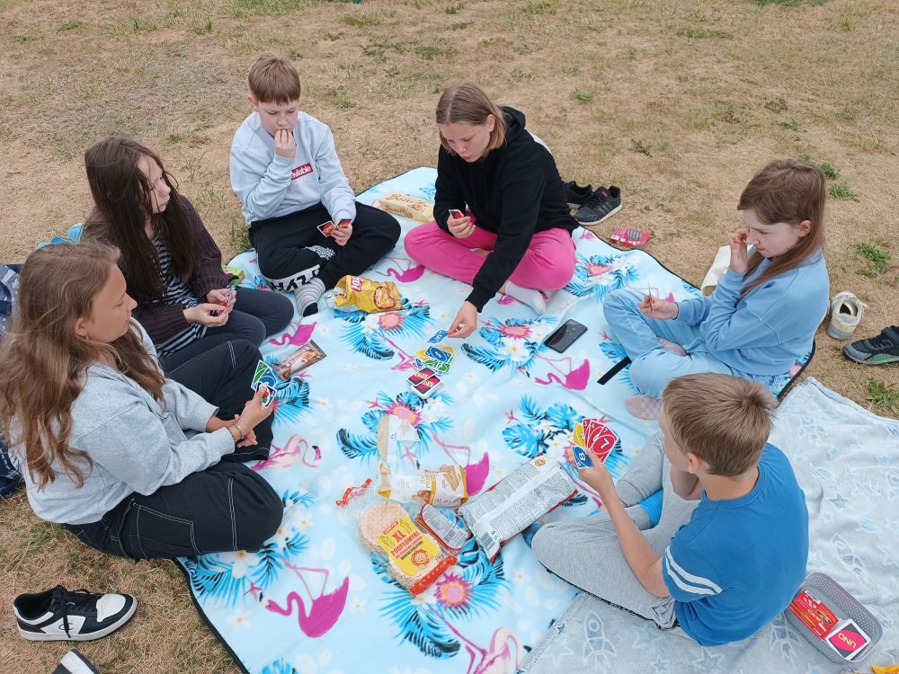 Uczniowie siedzą na kocu, jedzą smakołyki i grają w karty