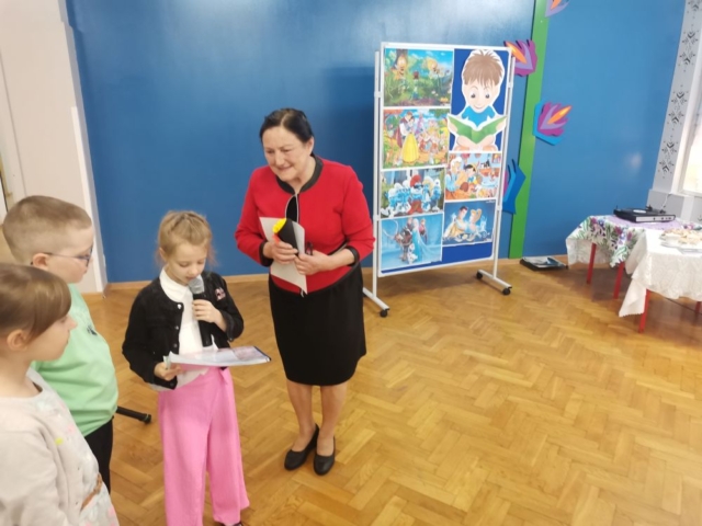 Przed panią Danutą Gronczyńską stoi troje dzieci i dziękuje pani wierszem i wręczonym dyplomem za odwiedzenie naszej szkoły