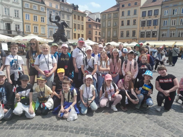 Dzieci stoją przy pomniku warszawskiej syrenki