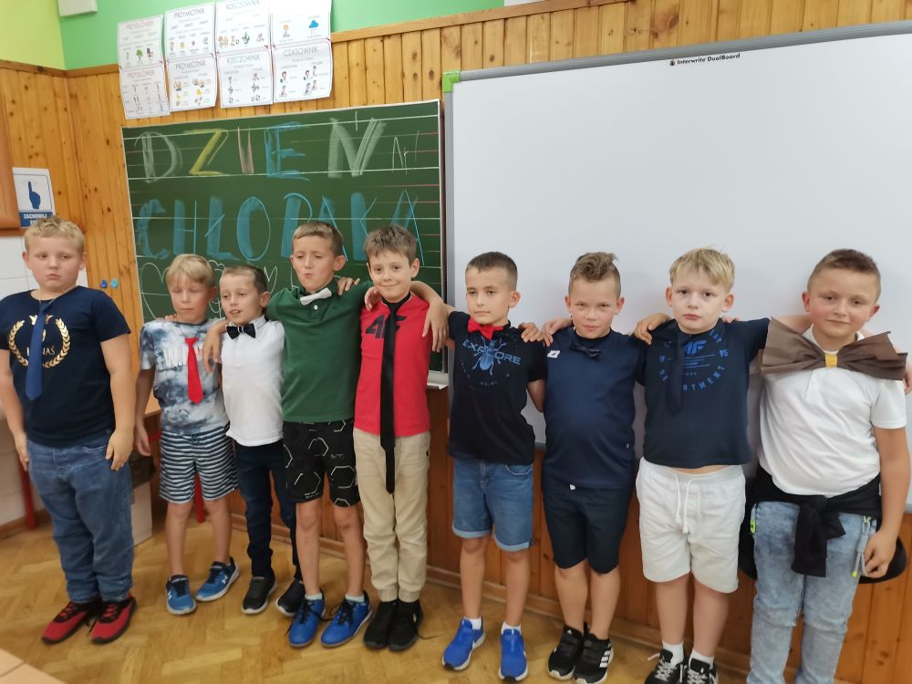 Chłopcy z klasy trzeciej stoją pod tablicą z napisem Dzień Chłopaka