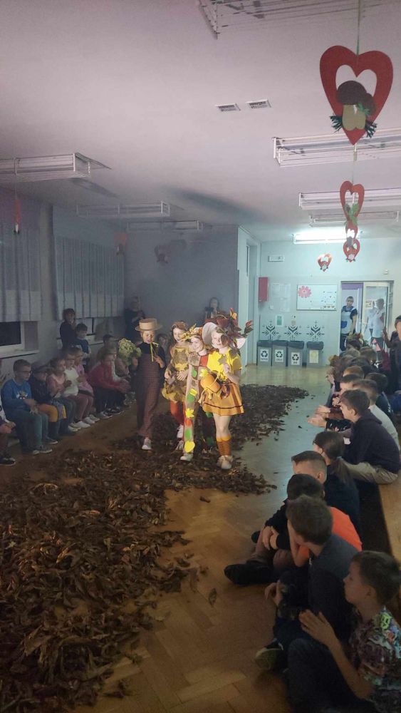 Cztery dziewczynki idą w strojach jesiennych po wybiegu z liści na pokazie mody.